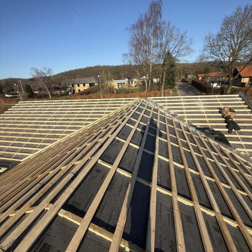 Tagopbygning med lægter og sort undertag på hus med blå himmel i baggrunden.