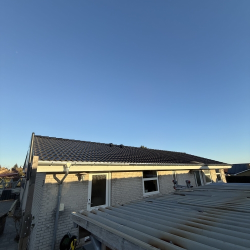 Ny tagbelægning monteret på hvid murermestervilla i lav sollys.