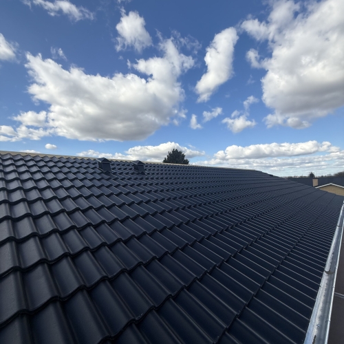 Sort tegltag med to ventilationshætter under blå himmel med skyer.