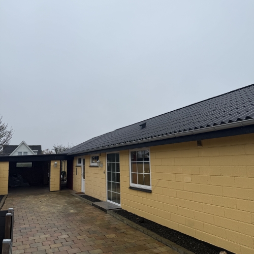 Nyrenoveret tag på gul husfacade med nyanlagt indkørsel i herregårdssten.