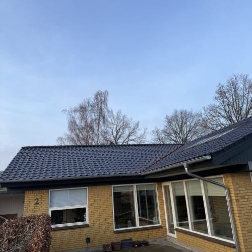 Færdig tagrenovering på gult murstenshus med ny tagbelægning og terrasse.