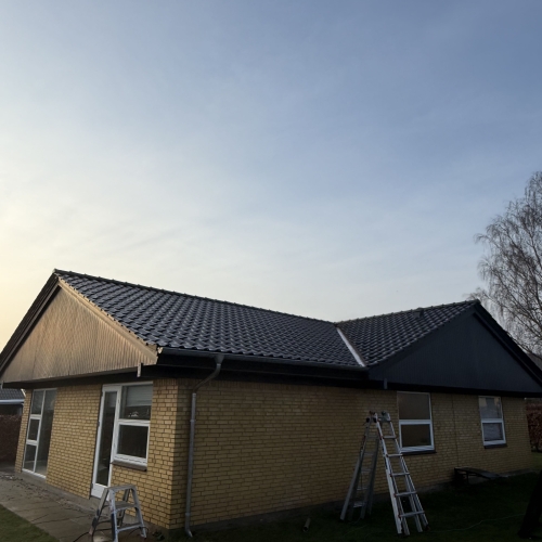 Nyopført sort tag på gul murstenshus med stilladser og stiger i haven.