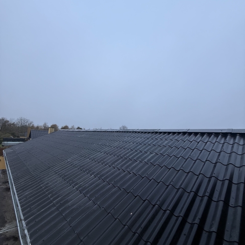 Stor sort stålpladetag på hus set fra tagryggen med let morgendis.