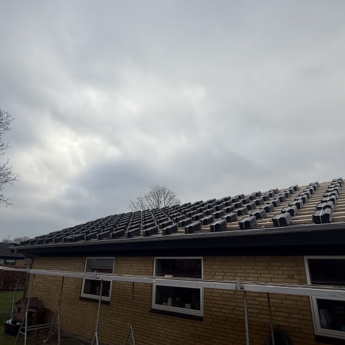 Tagrenovering i gang med sort tegl lagt klar på lægter på gul murstenshus.