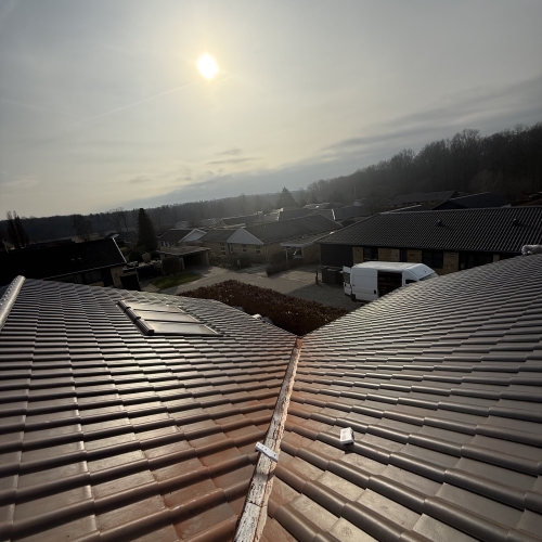 Tagrenovering set oppefra i solskin – nyt tag med ovenlysvindue og rygningssten.