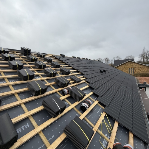 Oplægning af nye sorte tagsten under tagrenovering – tæt på detaljerne.