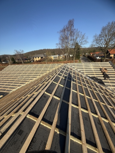 Tagopbygning med lægter og sort undertag på hus med blå himmel i baggrunden.