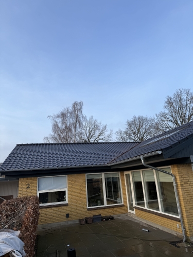 Færdig tagrenovering på gult murstenshus med ny tagbelægning og terrasse.
