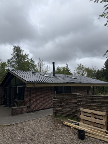 Tagrenovering med sortglaserede tagplader på fritidshus i skovområde